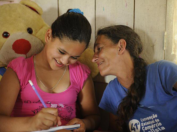 来自Projeto的照片Resgate  - 一名儿童在一本笔记本上写的，而一个成年妇女愉快地凝视着她